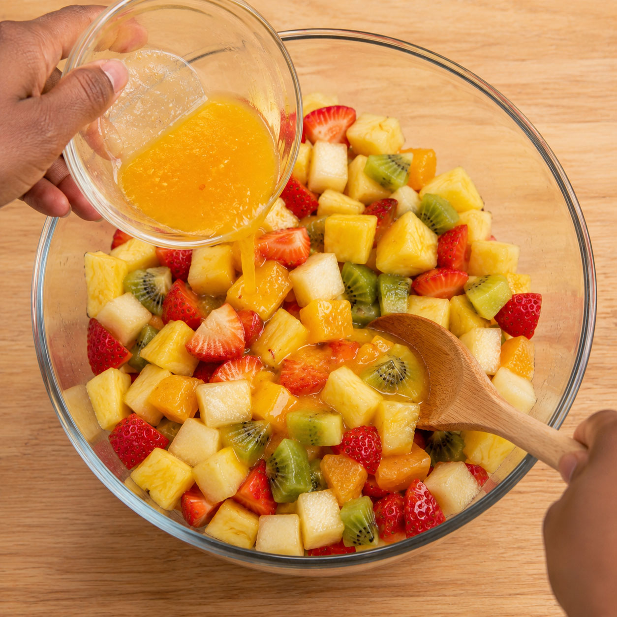 Pouring orange glaze over mixed fruit salad