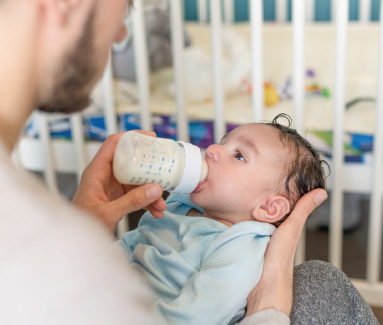 Baby sitting in high chair being fed with a spoon.