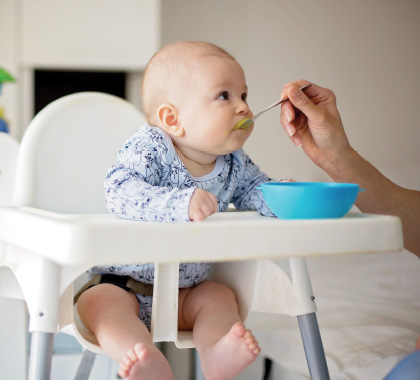 Baby in a high chair being fed with a spoon from a blue bowl.