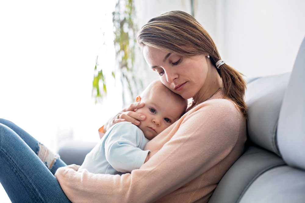 Woman holding a baby tenderly on a couch.