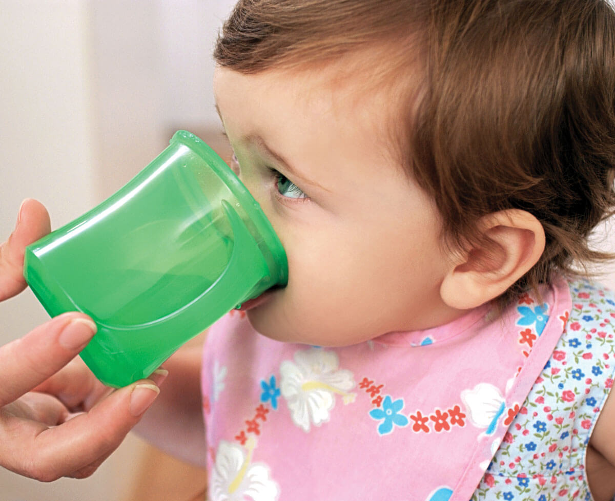 Toddler drinking from green cup, wearing a floral bib.