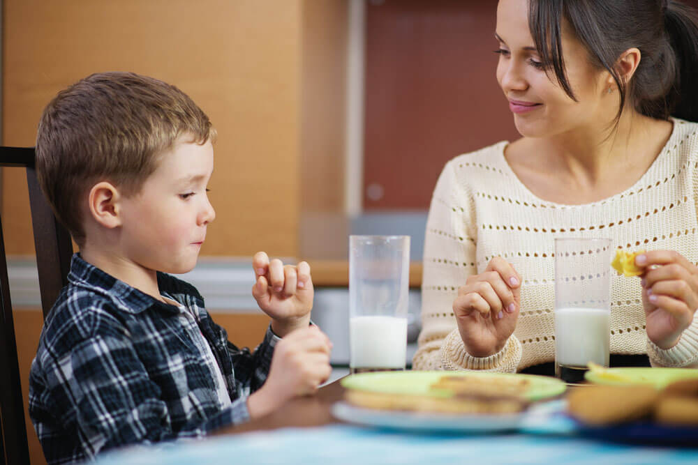 Mother and child enjoying a snack together at a table, with glasses of milk and plates of food.