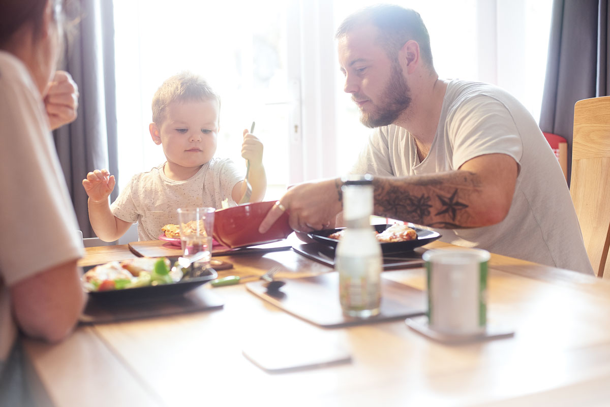 Father and child seated at a table, sharing a meal together in soft daylight.