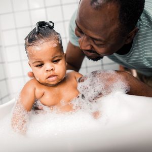 DadBathingBaby Father gently bathes baby in tub, surrounded by bubbles.