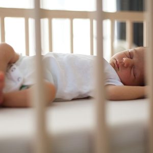 NewbornSleepInCrib Sleeping baby in a crib with arms raised, peaceful and surrounded by soft light.